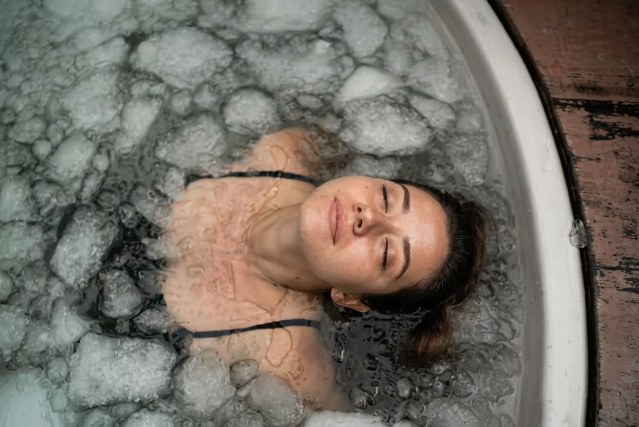 A person lying back in an ice bath filled with ice cubes