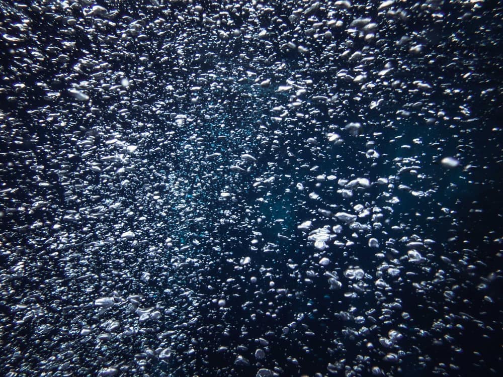 Captivating view of countless bubbles rising underwater against a deep blue background.
